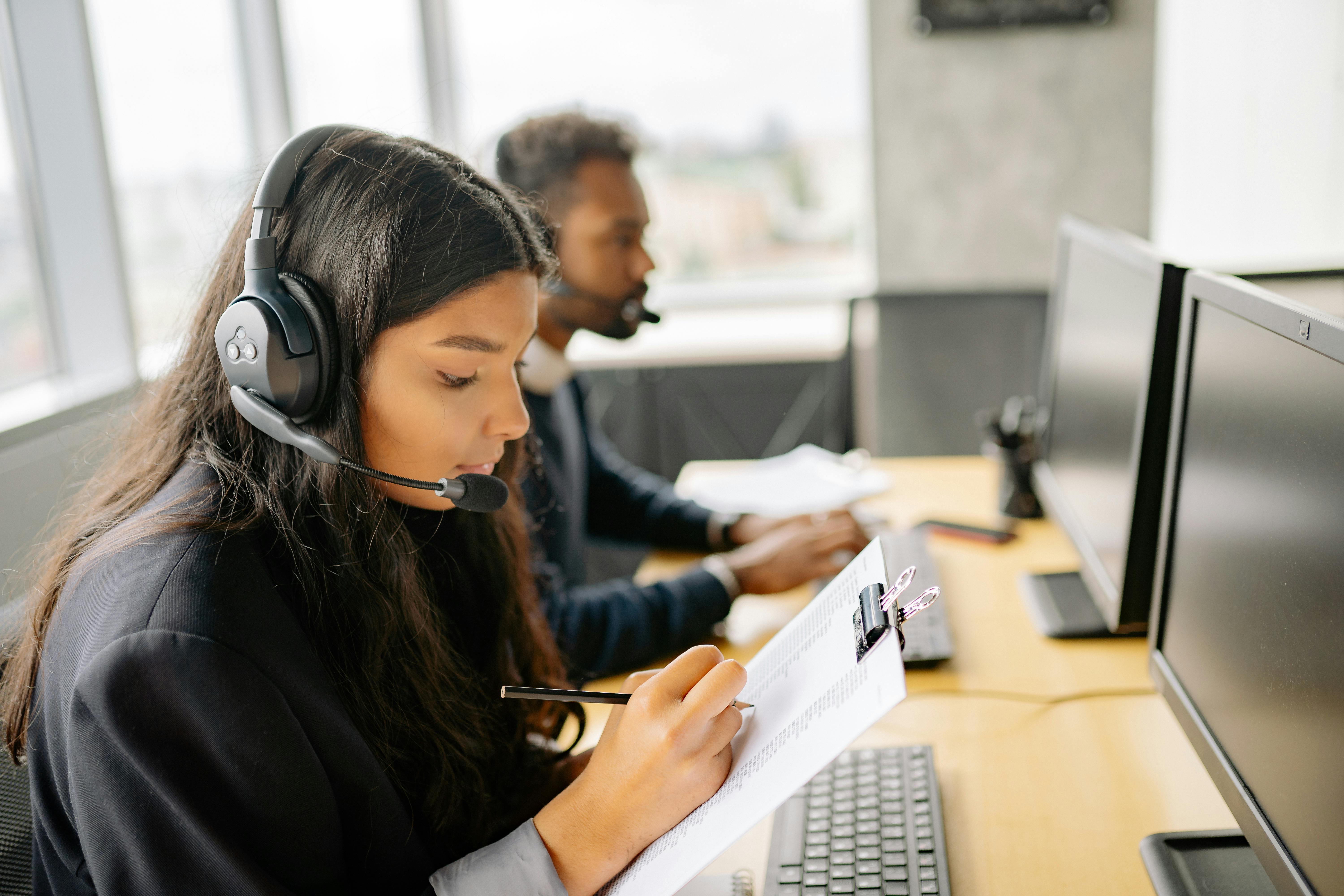 a man and woman sitting in front of computer monitors talking on headsets.